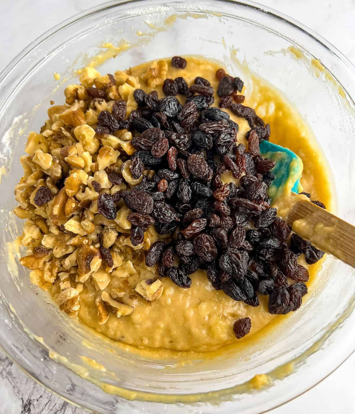 Folding in the walnuts and raisins into the batter mixture using a spatula.