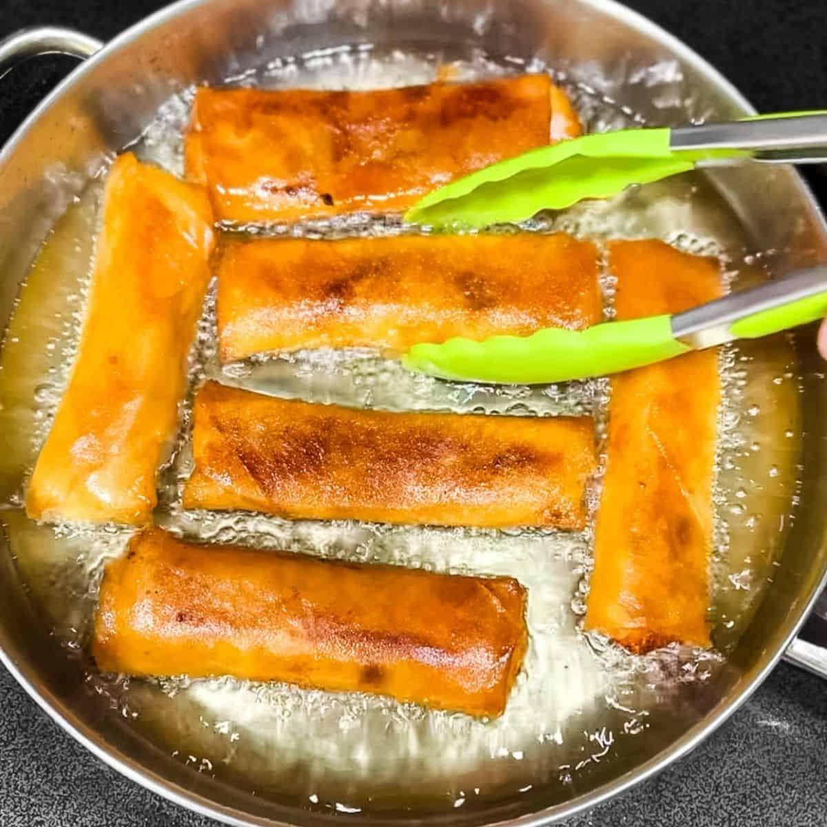 Frying the beef lumpia in a skillet until golden brown and crispy.