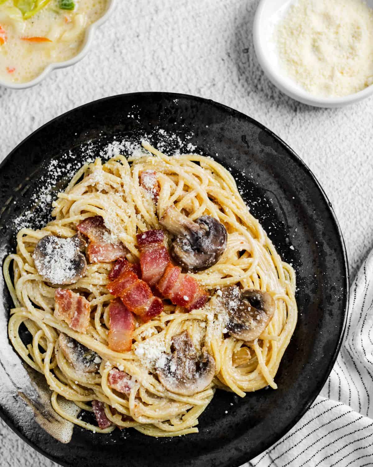 Finish dish of carbonara on a black plate in a table.