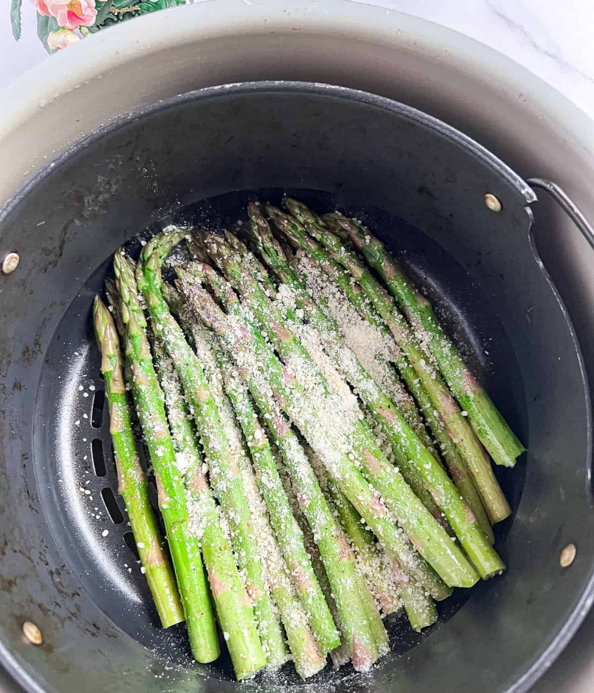 Preparing to air-fry the asparagus in the basket with seasonings and parmesan cheese on top.