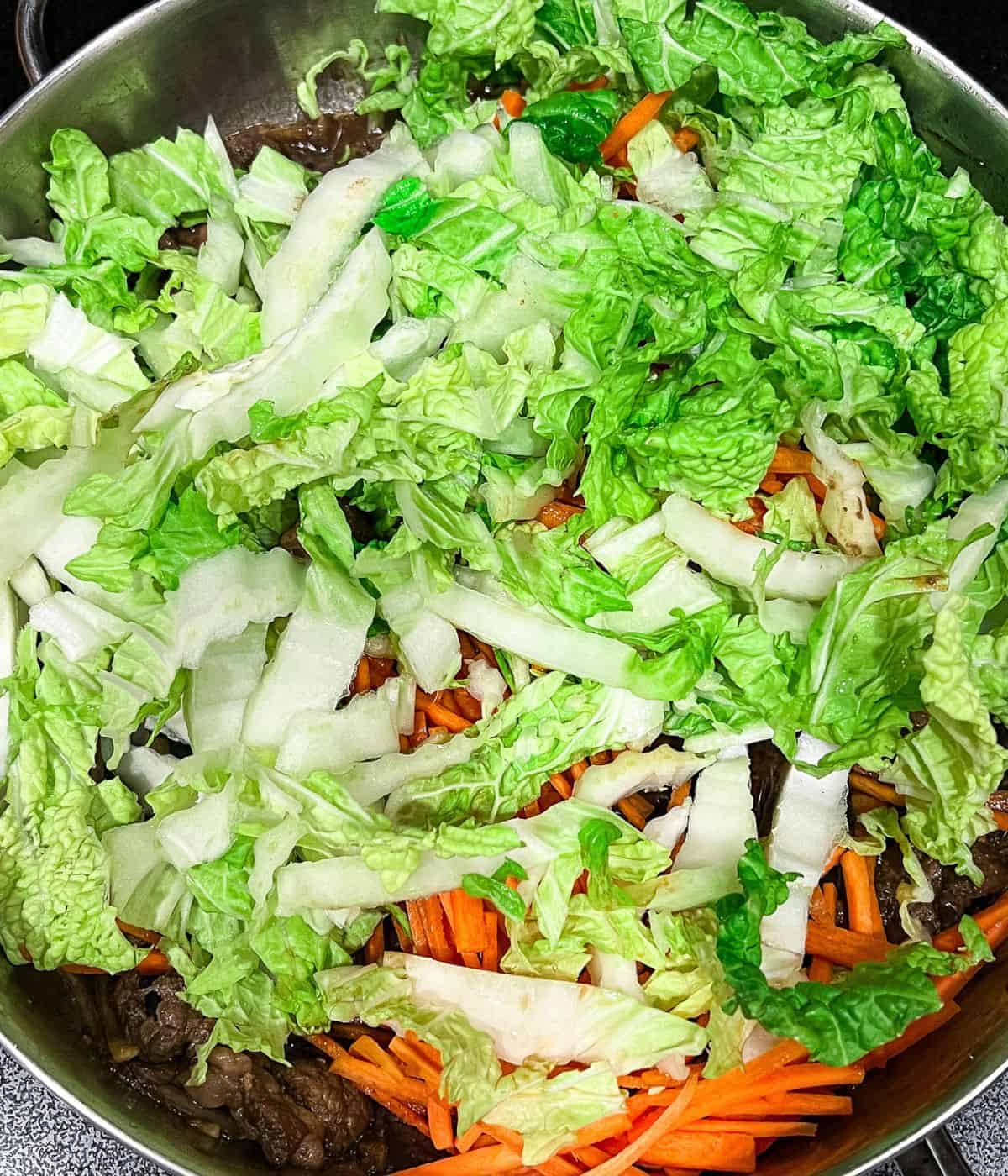 Adding carrots and napa cabbage to beef udon stir-fry.