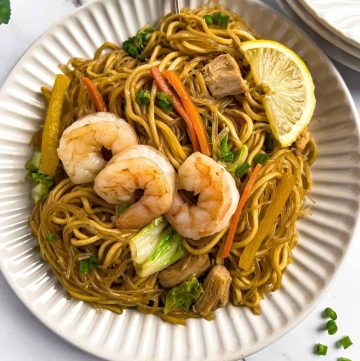 Pancit bihon and canton noodle dish in a plate with a slice of lemon.