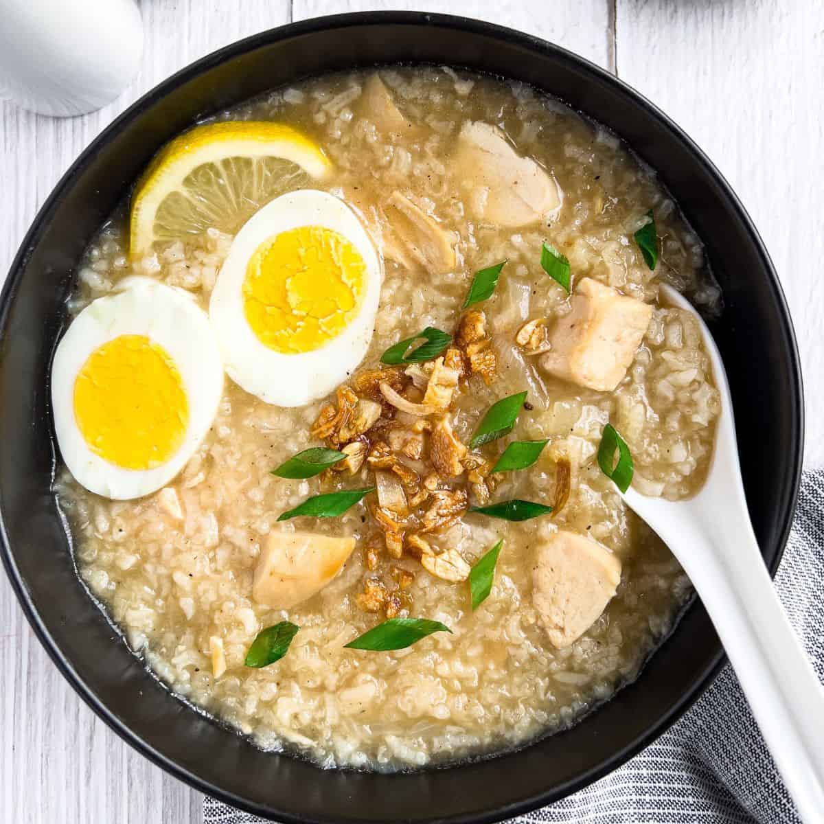 Arroz caldo in a bowl with slices of egg, lemon, chopped green onion and toased garlic.