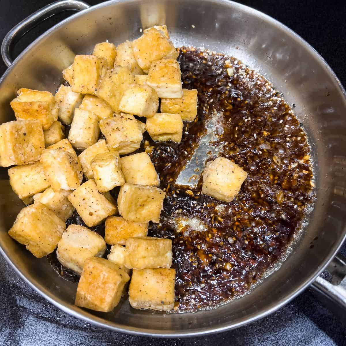 Adding to fried tofu to the skillet and coat it with the sweet and sticky sauce.