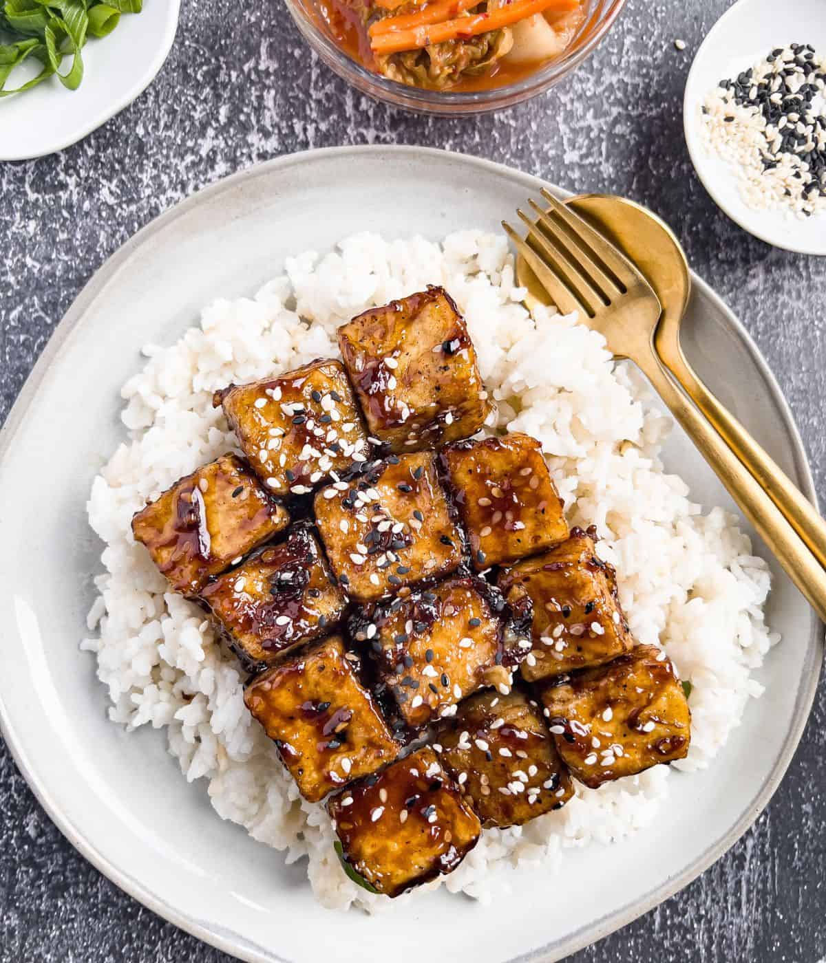 Finish dish of sweet sticky and sesame tofu on the table with kimchi in the side.