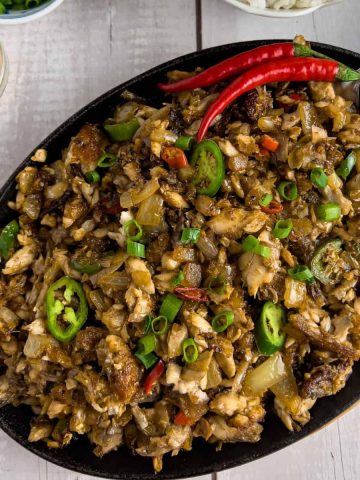 Finish dish of bangus sisig in a sizzling platter with red chili, chopped green onions and rice.