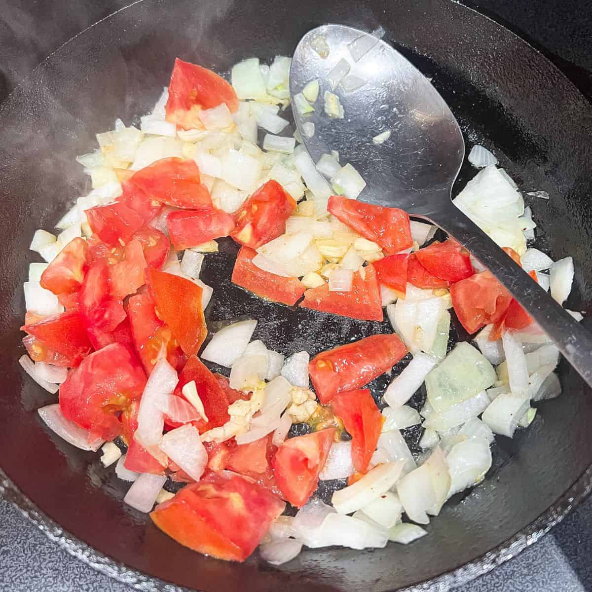 Cooking onion, garlic, and tomatoes in a skillet.