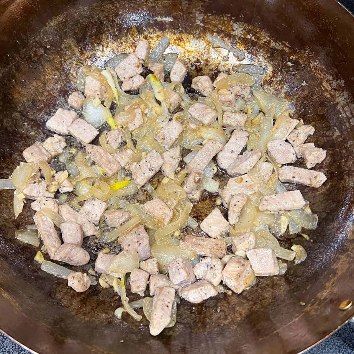 Cooking onion, garlic and pork loin in a wok.