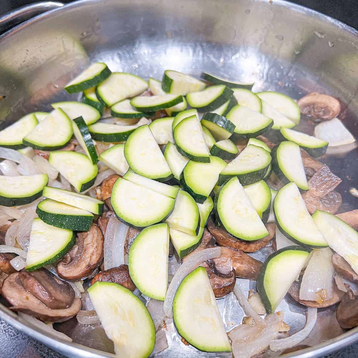 Adding zucchini into the skillet.