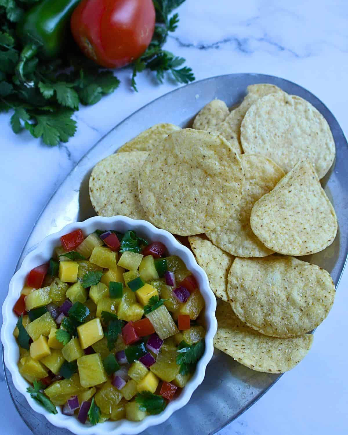 Mango pineapple pico de gallo salsa in a bowl with tortilla chips.