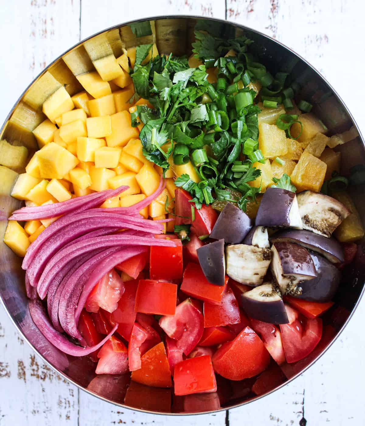 Mango, pineapple, tomatoes, red onions, cilantro and green onions in a bowl.