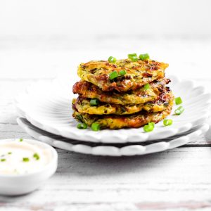Stacks of air fried zucchini fritters in a plate with a dipping sauce.