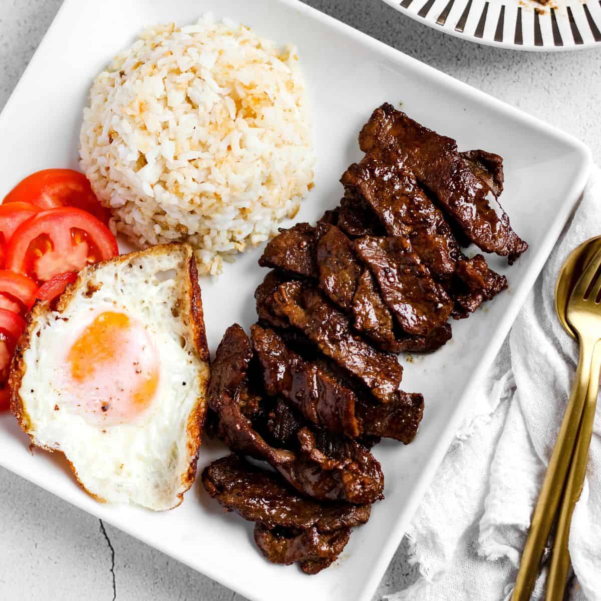 Finish dish of beef tapa in a plate with garlic fried rice and egg.