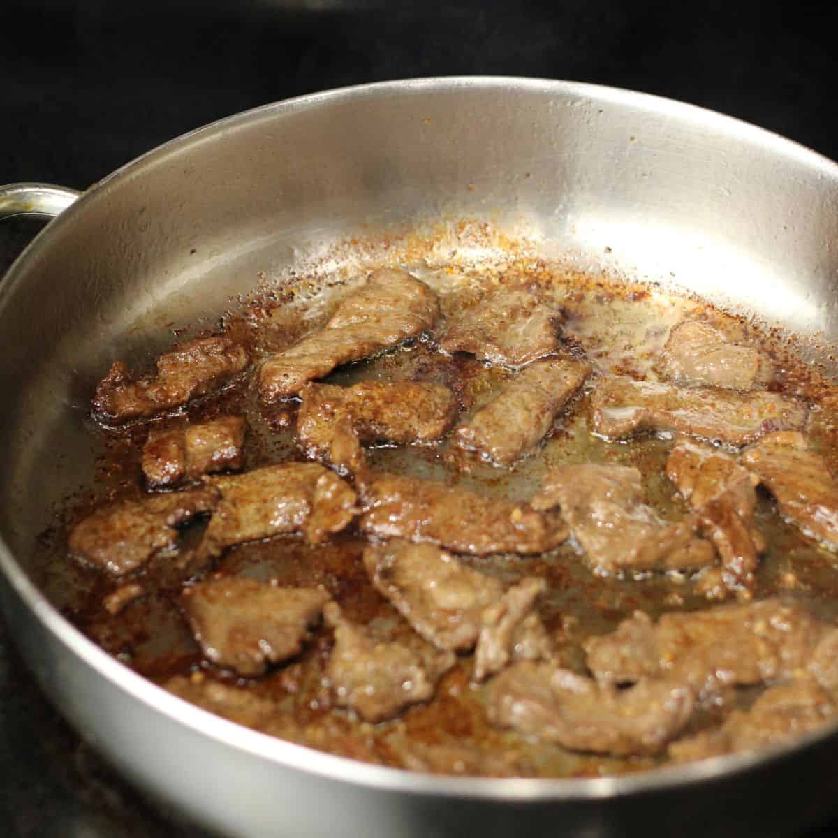 Frying the beef tapa until it is seared and caramelized.