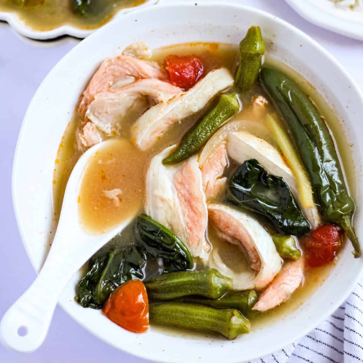 A bowl of salmon belly sinigang with a spoon.