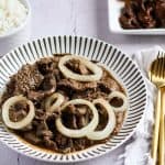 Finish dish of bistek tagalog in a plate with rice in the side.