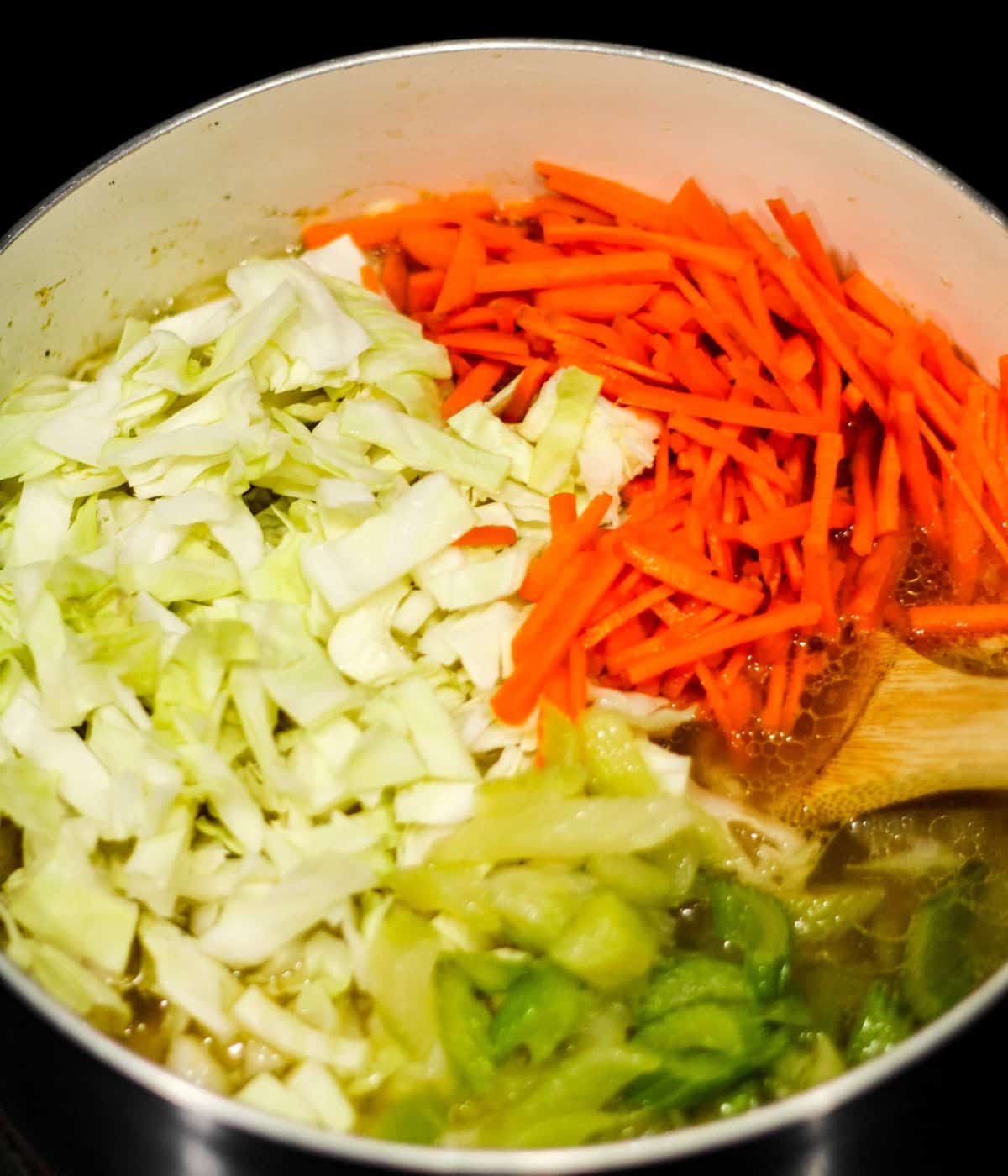 Cooking carrots, celery, and cabbage into the dutch oven.