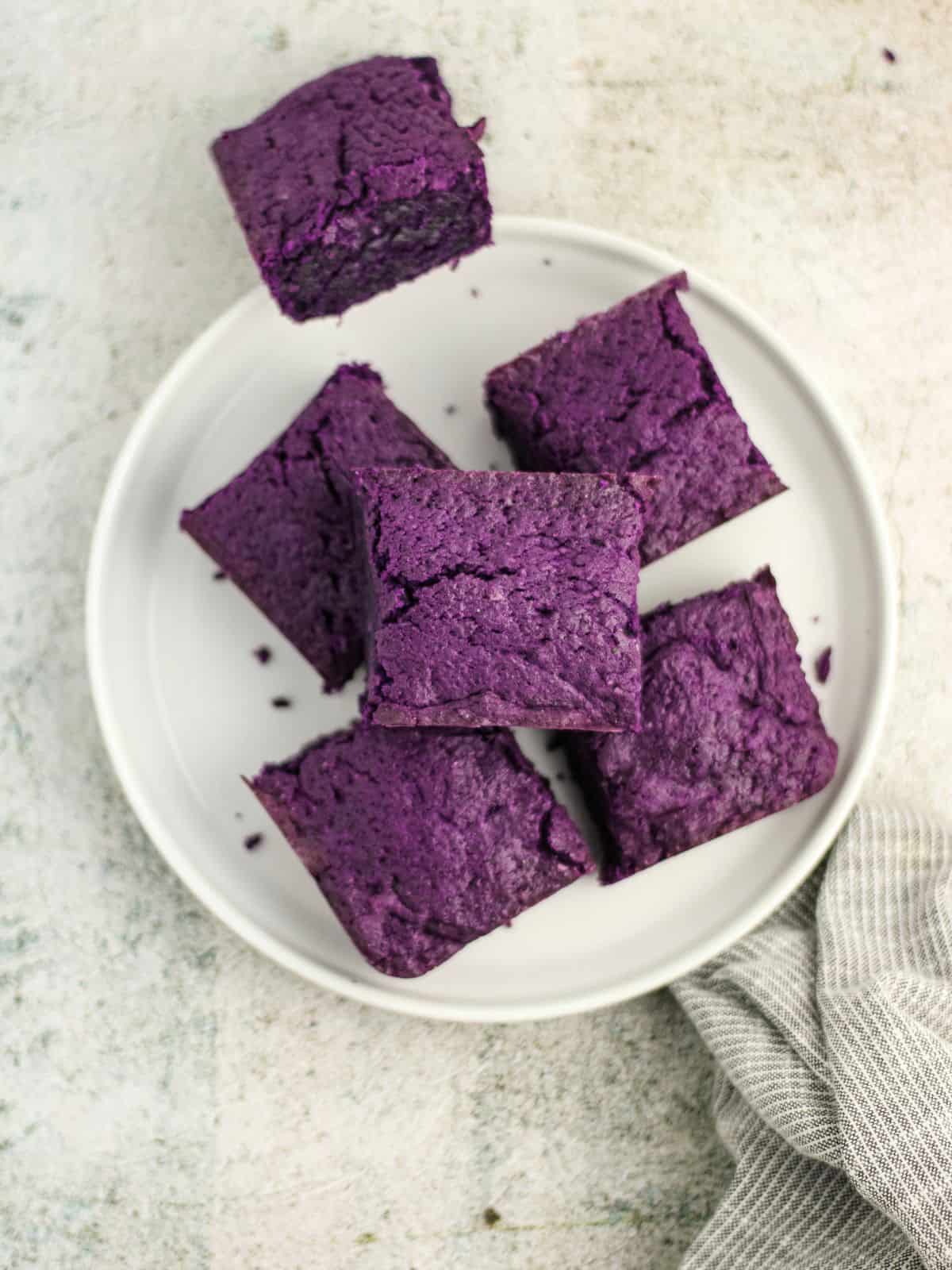 Slices of ube brownies on a plate in a table.