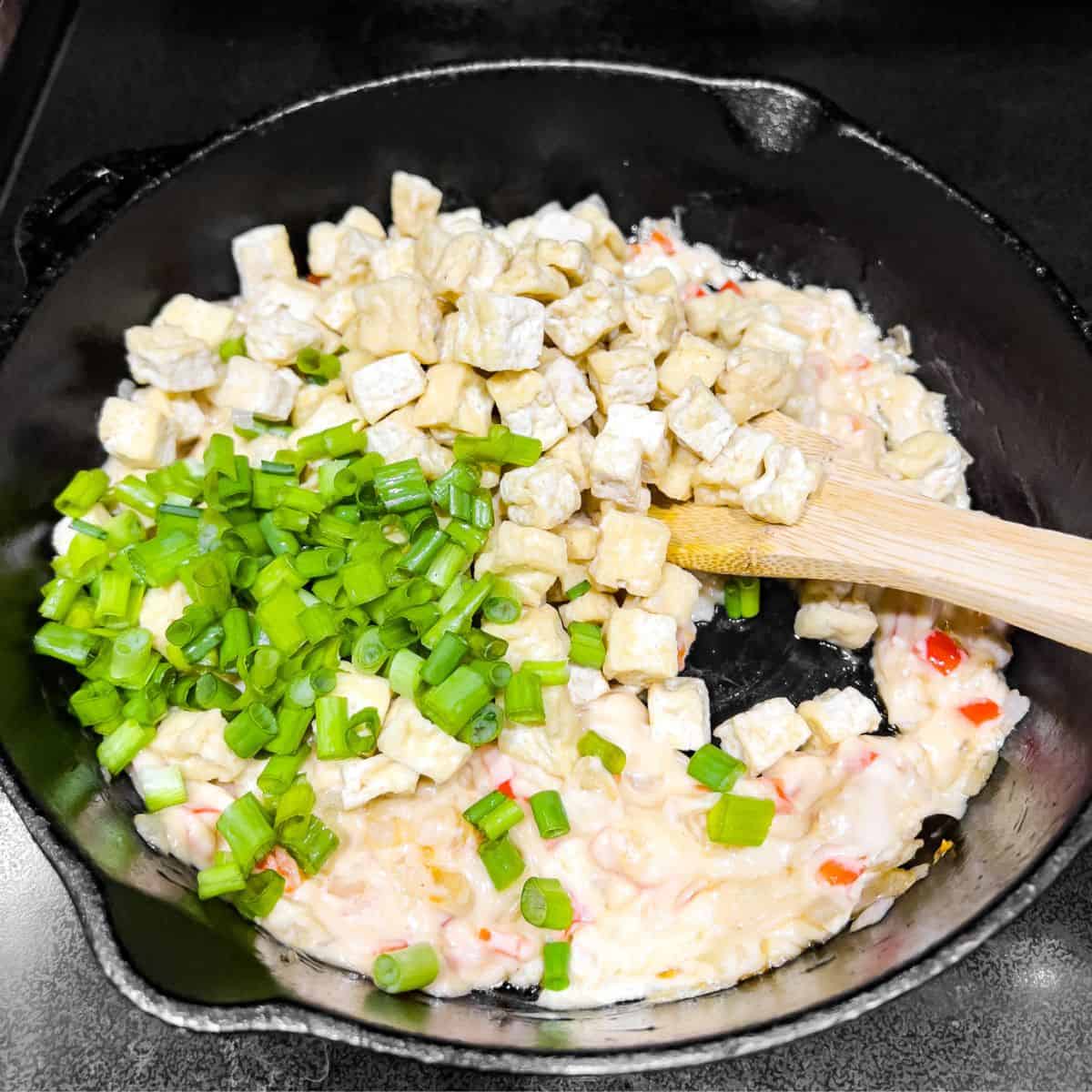 Adding tofu and green onion in the skillet.