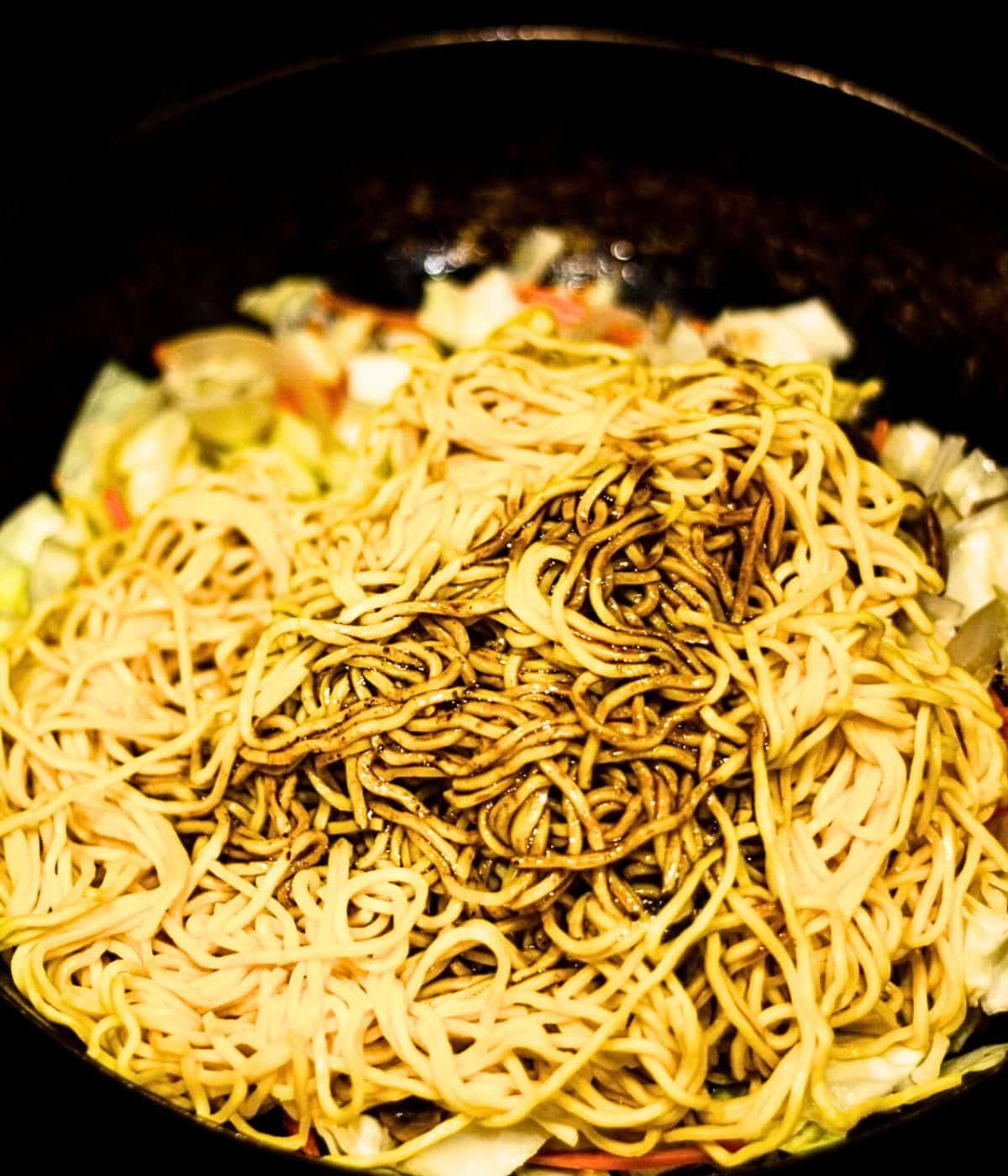 Adding yakisoba noodles and sauce to the dish.