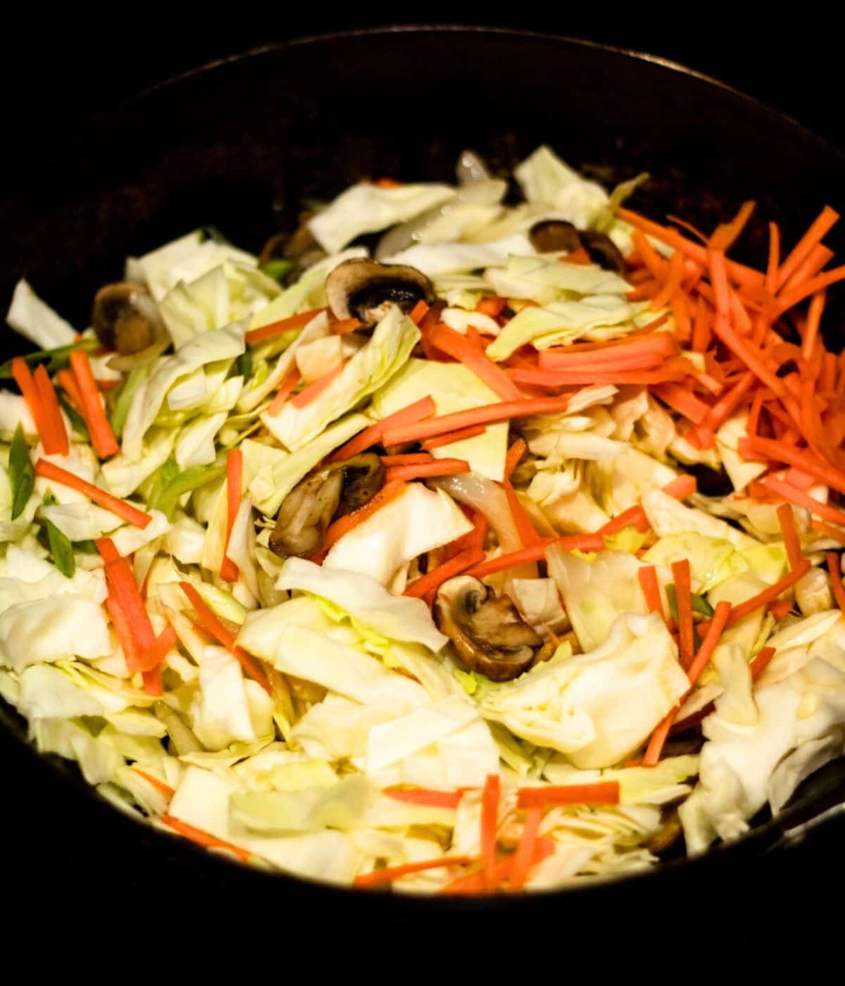 Adding cabbage and carrots to the wok.