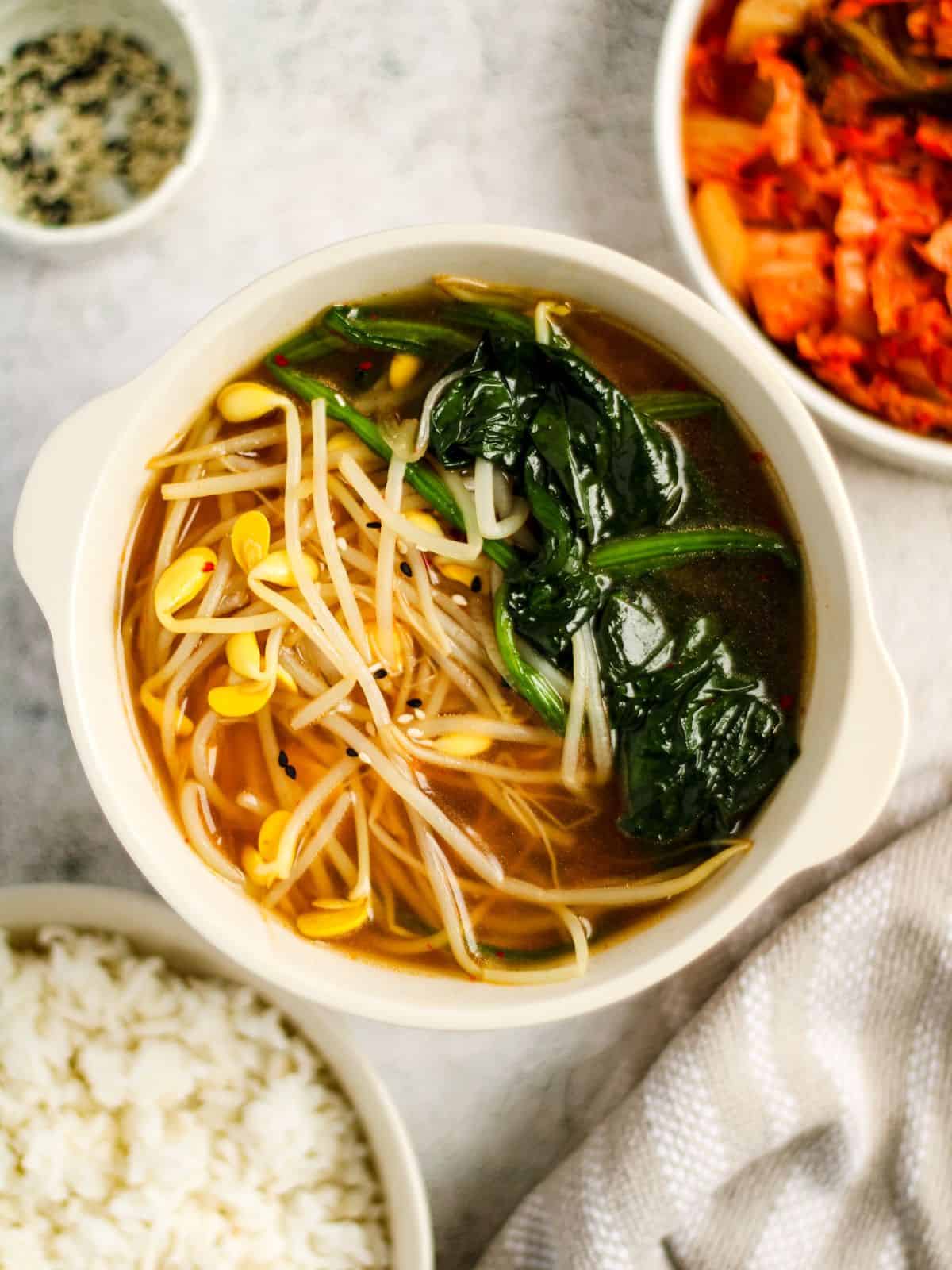 Korean spinach soup in a bowl with a side of rice and kimchi.