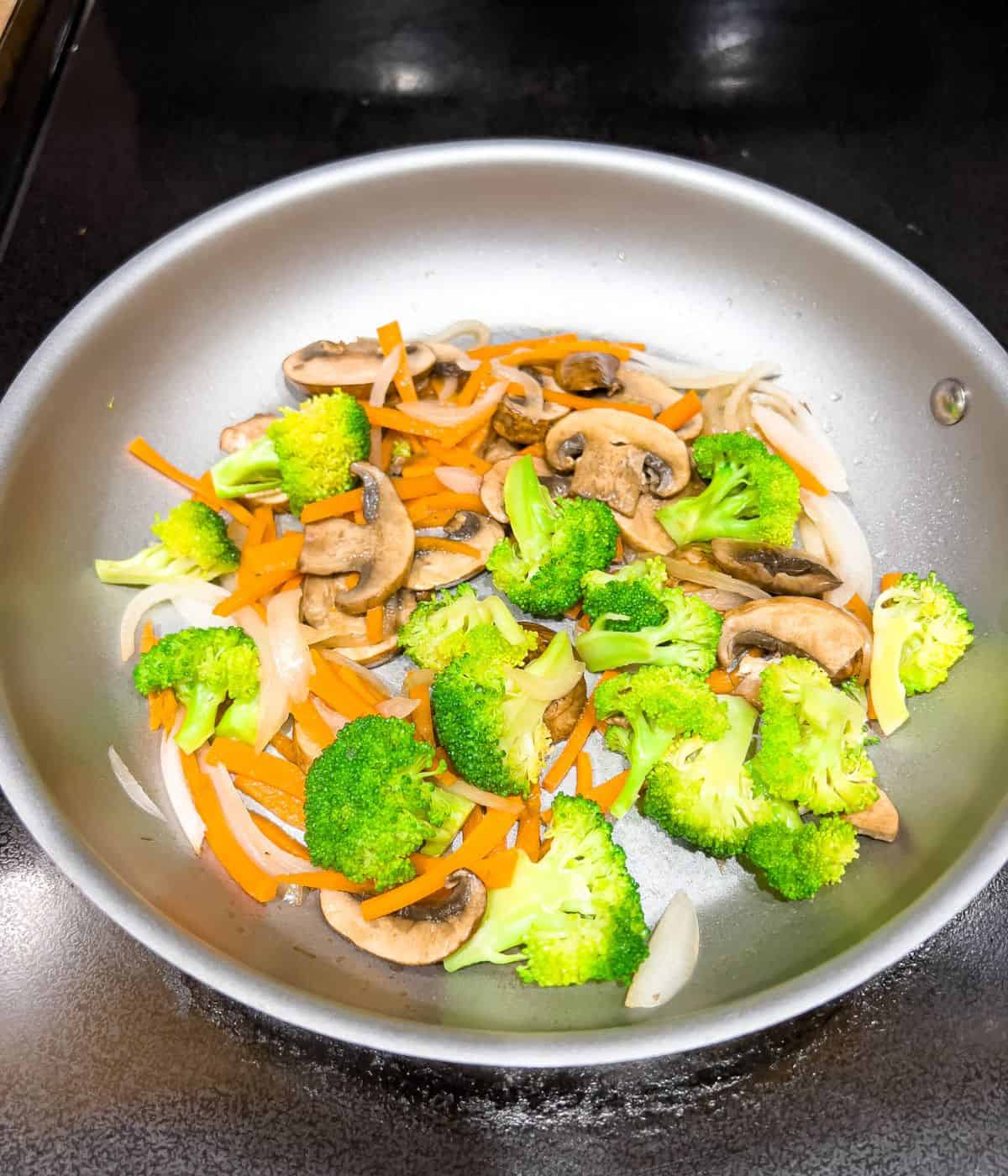 Stir-frying carrots, broccoli, and mushrooms in a skillet.